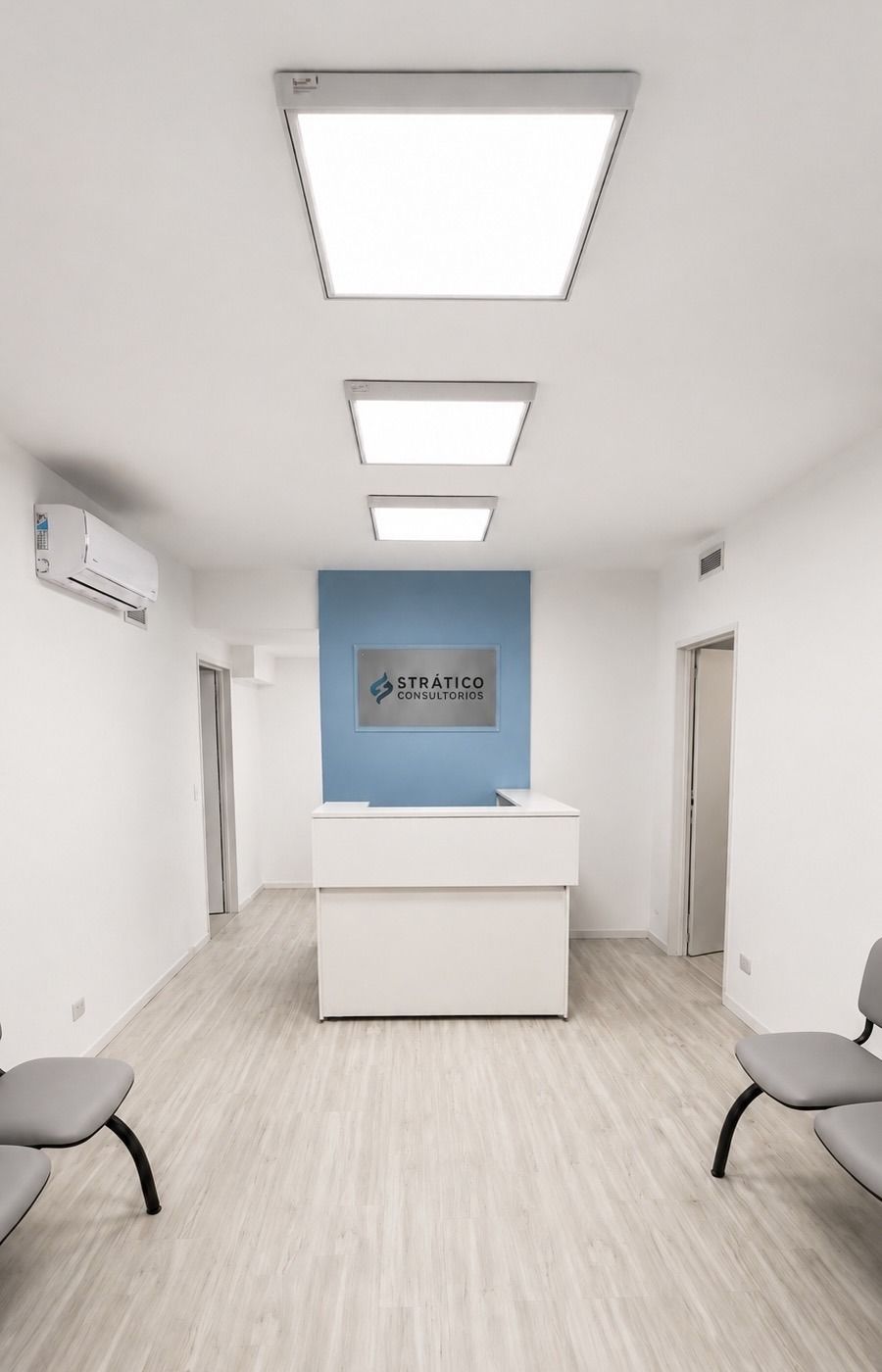 La recepción del consultorio: el pasillo iluminado, el mostrador blanco frente a la pared celeste con el logo de Strático y las sillas de la sala de espera